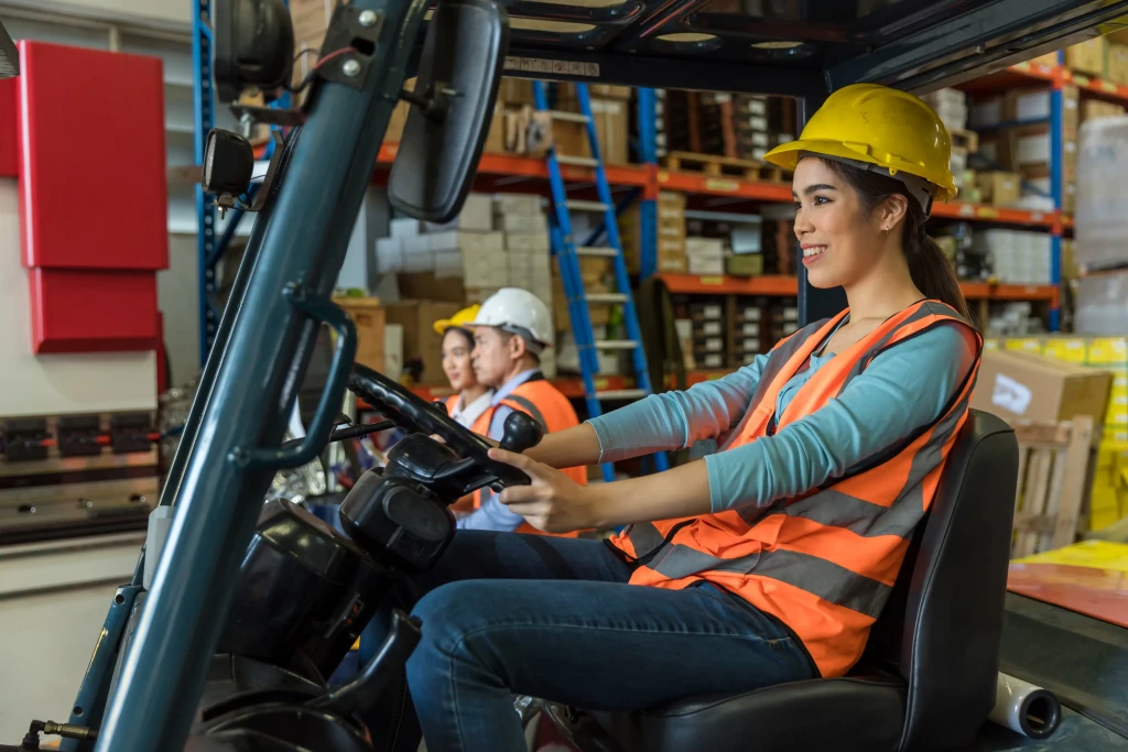 Azjatka w ubraniu roboczym prowadzi wózek widłowy w magazynie